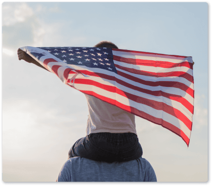 Person holding American flag outdoors during sunset.
