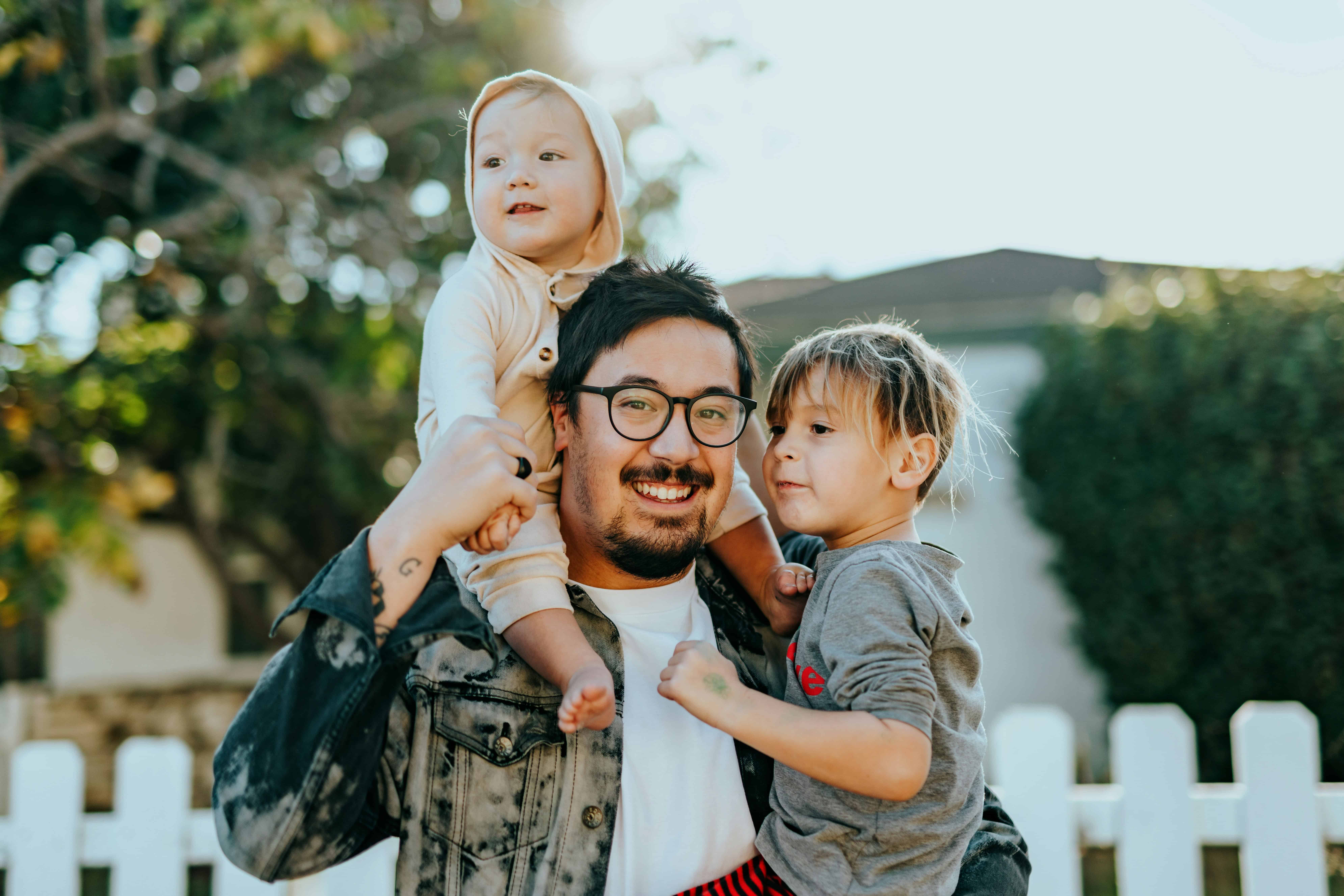 Family with children playing outside in a sunny yard, smiling and enjoying quality time together.
